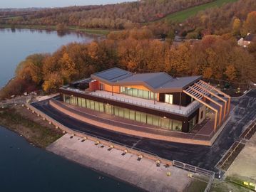 Modern building with large windows by a lakeside surrounded by autumn trees.