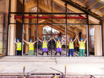 Construction workers in safety gear holding hands inside a wooden framed building.