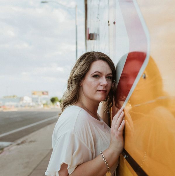 Woman leaning against a reflective yellow surface on a city street.