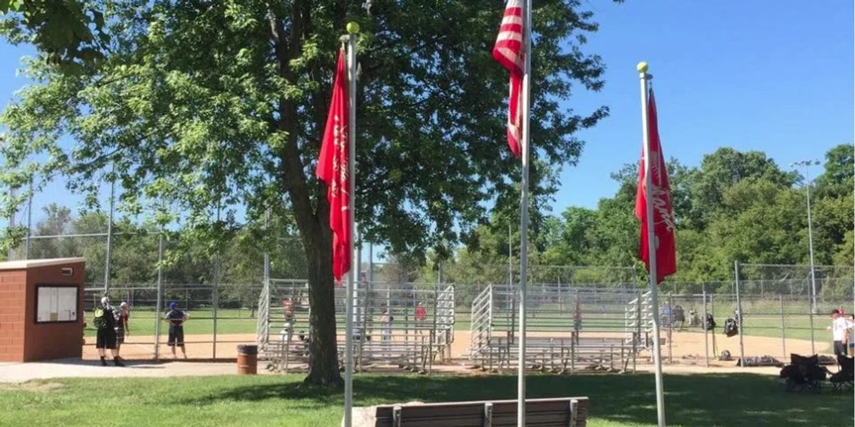 Flags and people at a baseball field on a sunny day.