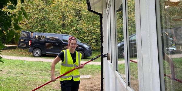 woman in high vis holding window cleaning pole with brush on window. window cleaning. sparkle clean.