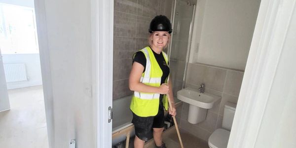 woman in high vis and hard hat sweeping floor in bathroom. construction cleaning. builders cleaning.