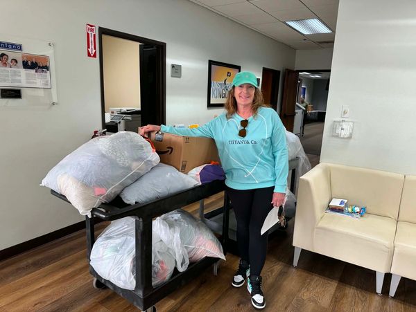 Woman standing next to cart filled with bags and boxes indoors.