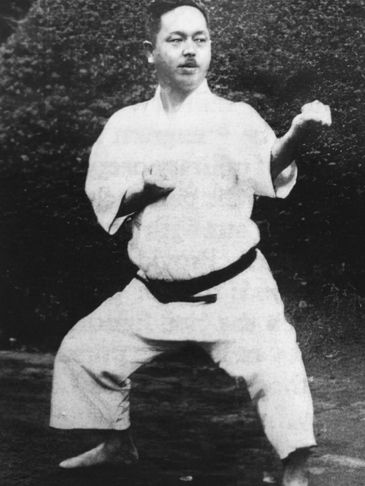 A man in a karate gi practicing a martial arts stance outdoors.