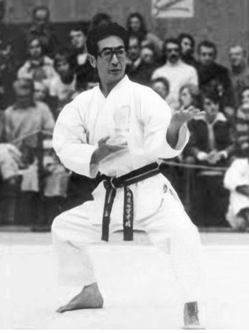 Martial artist in traditional gi performing kata with spectators watching.