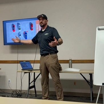 Man presenting in a conference room with visuals on a screen.
