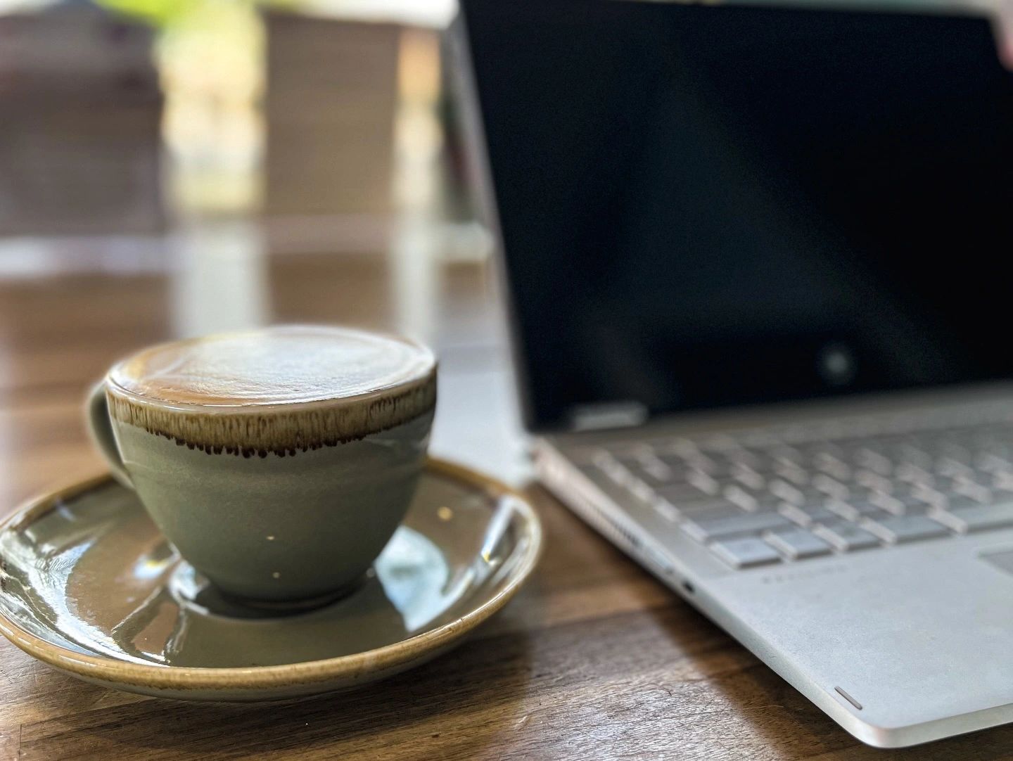 A coffee cup with latte art next to a laptop on a wooden table.
