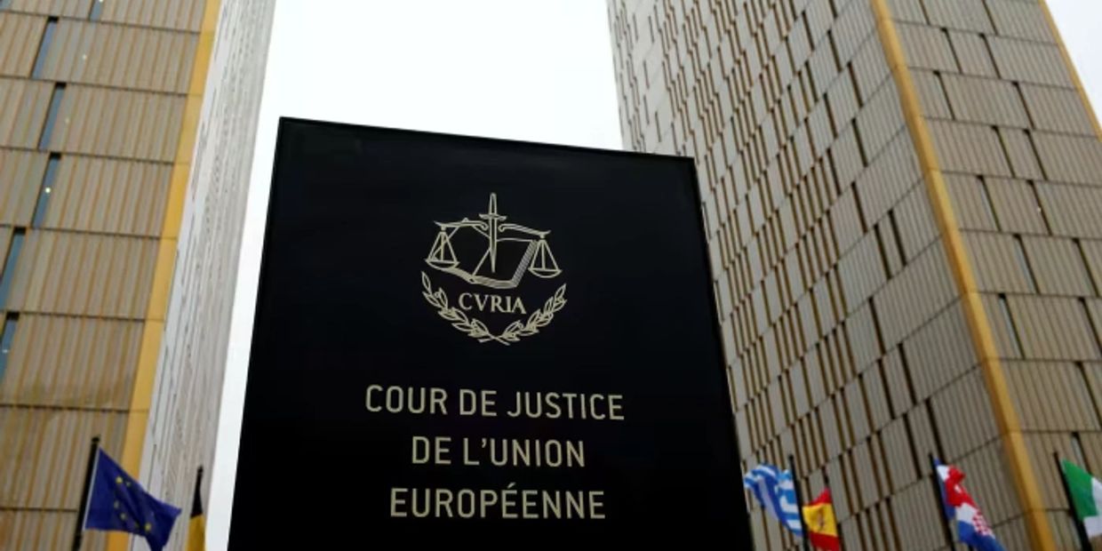 Signboard of the Court of Justice of the European Union with surrounding flags and buildings.