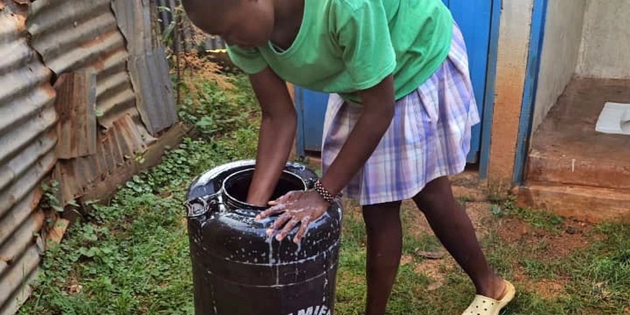 A girl washing hands in a large black container outdoors.