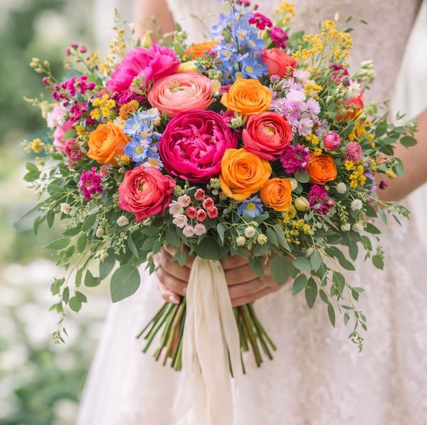 A vibrant bridal bouquet with pink, orange, blue, and yellow flowers.
