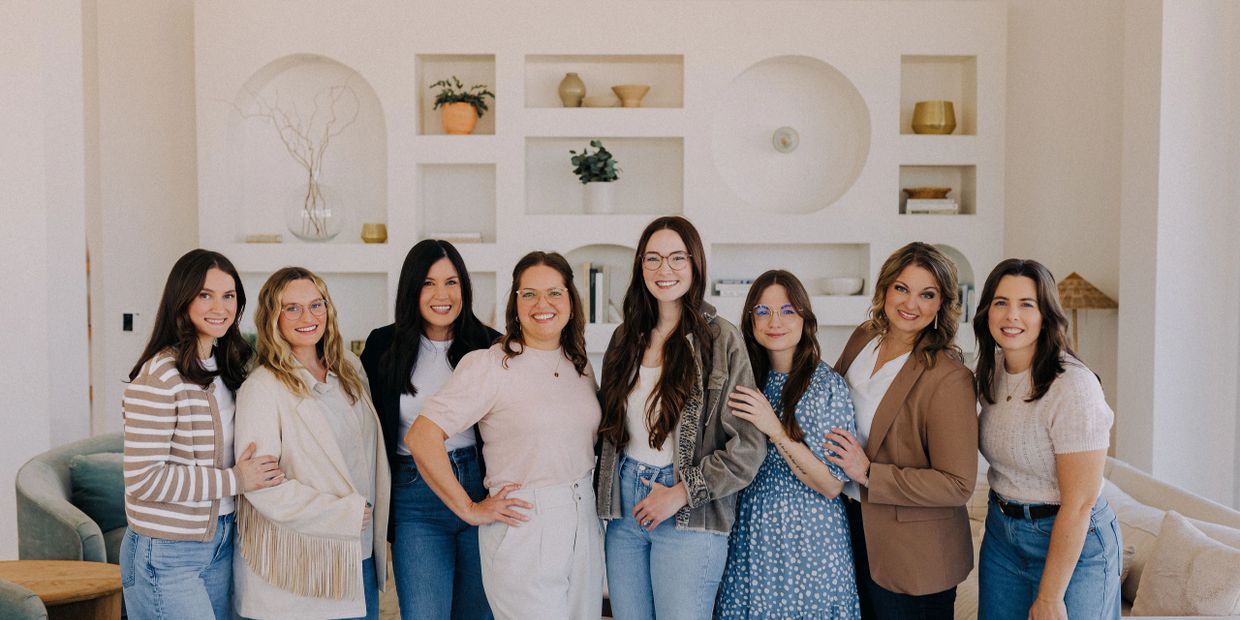 A group of eight smiling women posing together indoors.