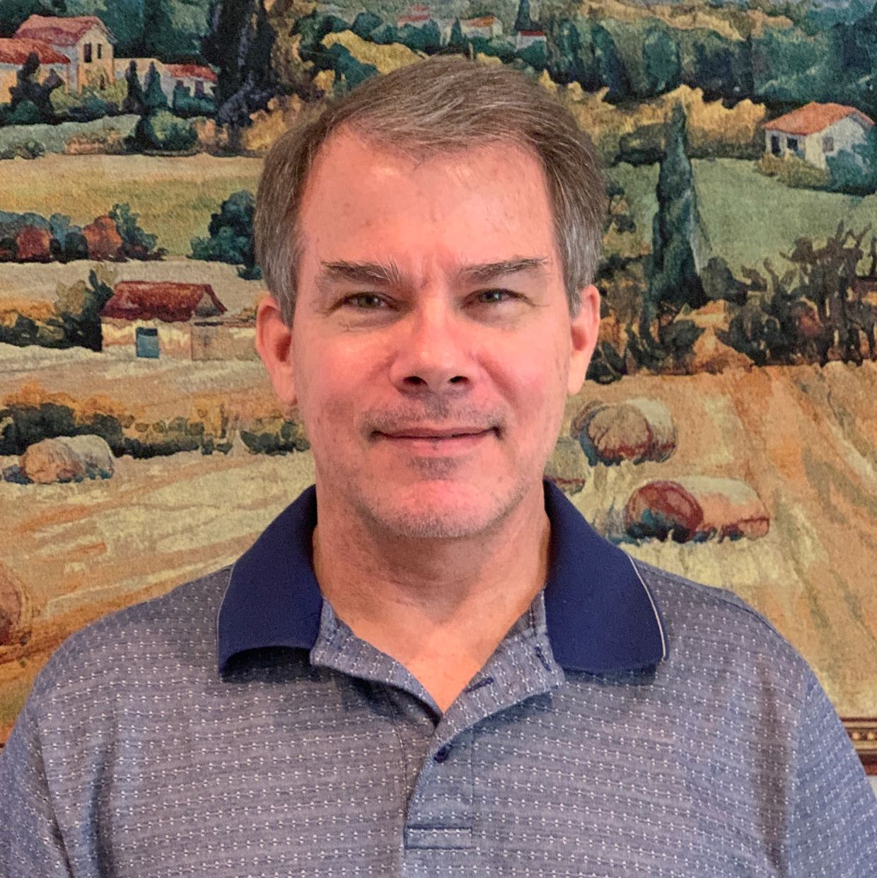 Middle-aged man smiling in front of a countryside painting.