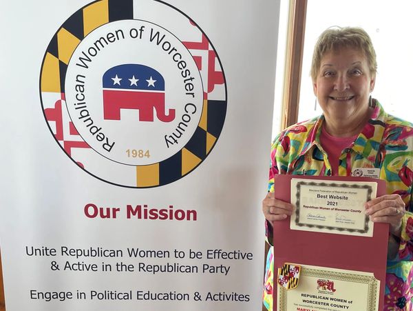 Woman holding an award next to a Republican Women of Worcester County banner.