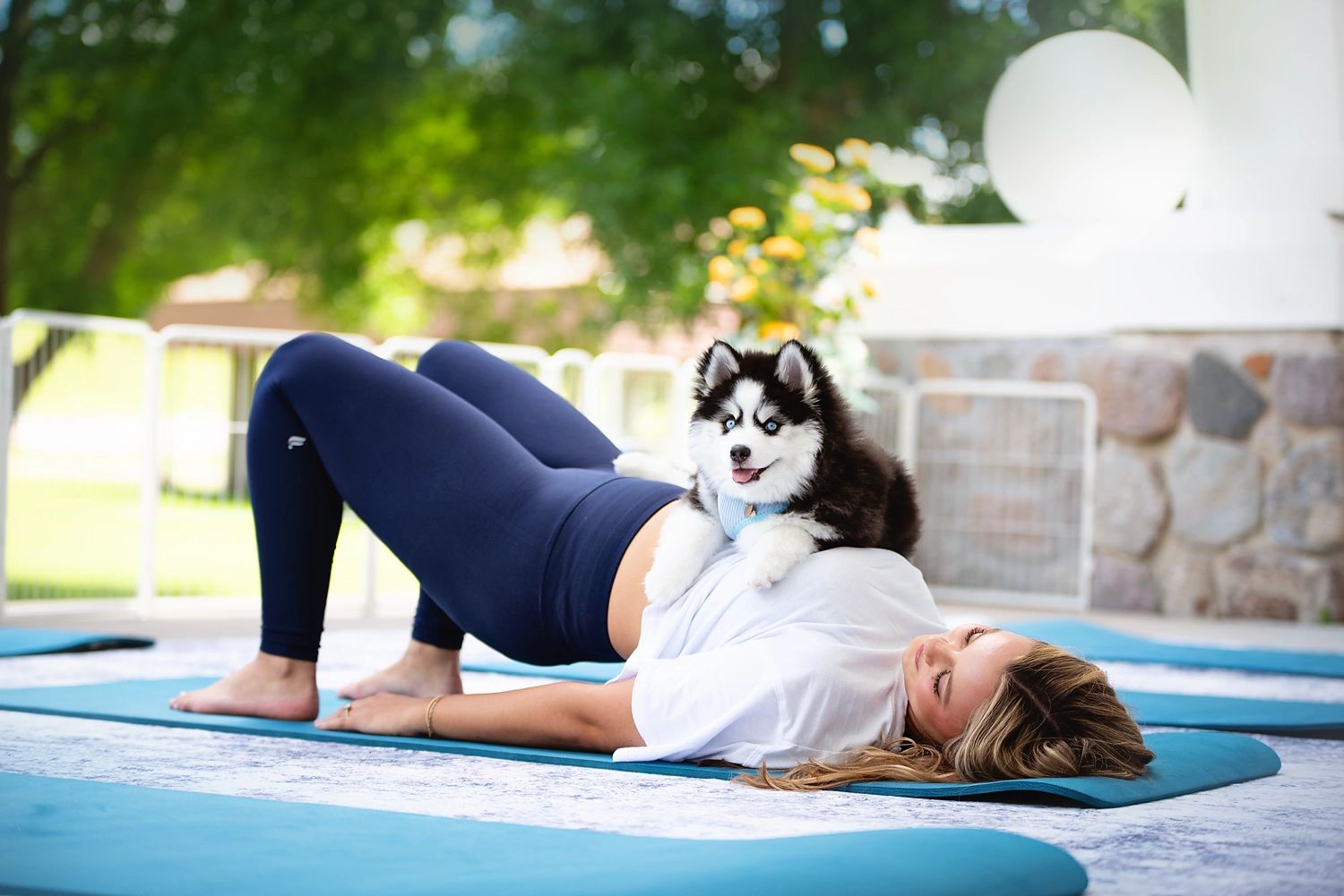 Woman doing yoga with a husky puppy on her stomach.