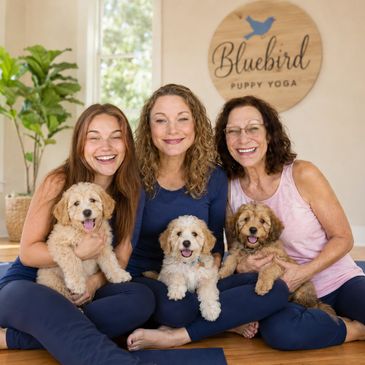 Three women happily holding puppies at Bluebird Puppy Yoga.