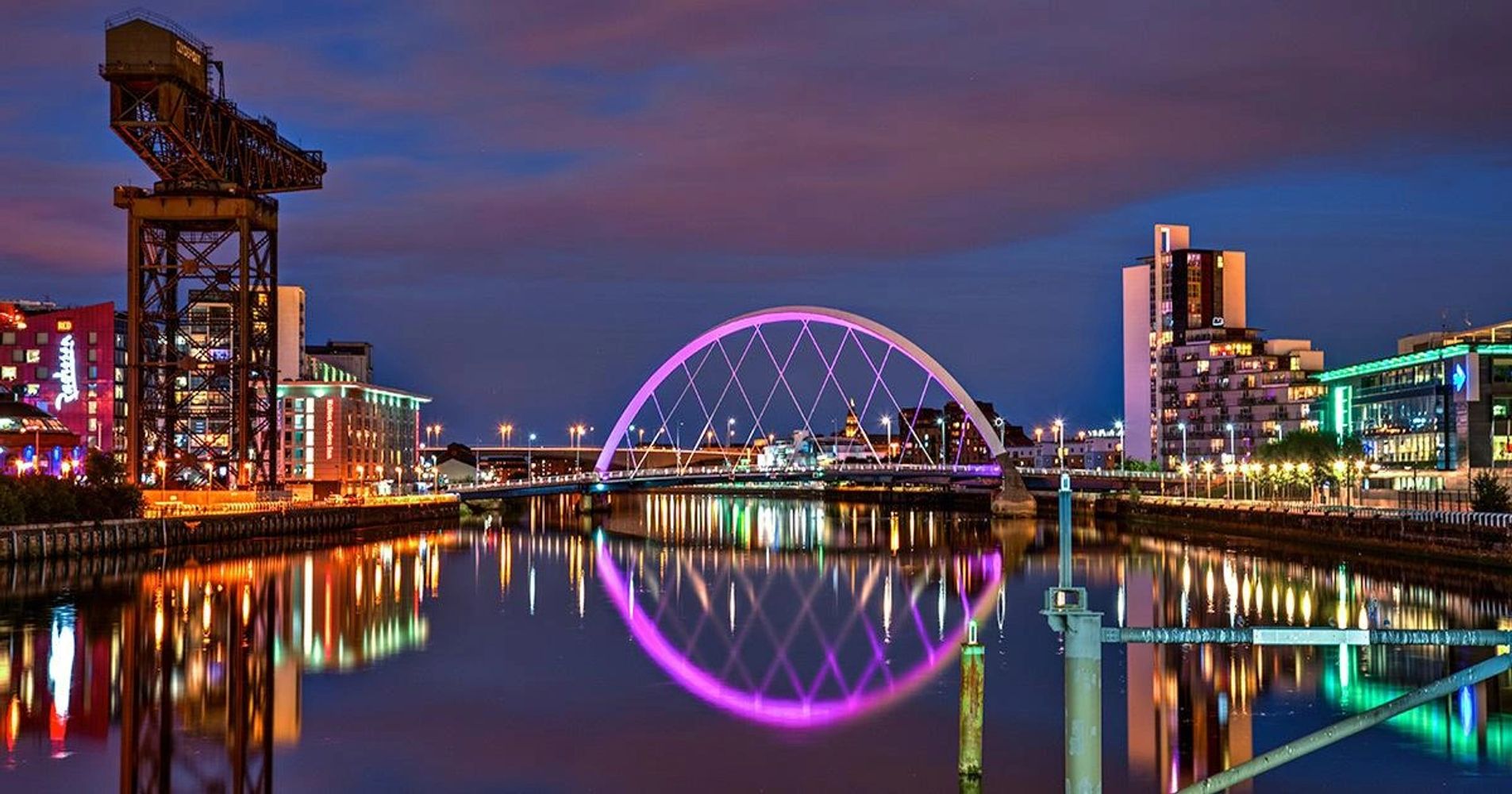 Night view of a city bridge with colorful lights reflecting on the water.