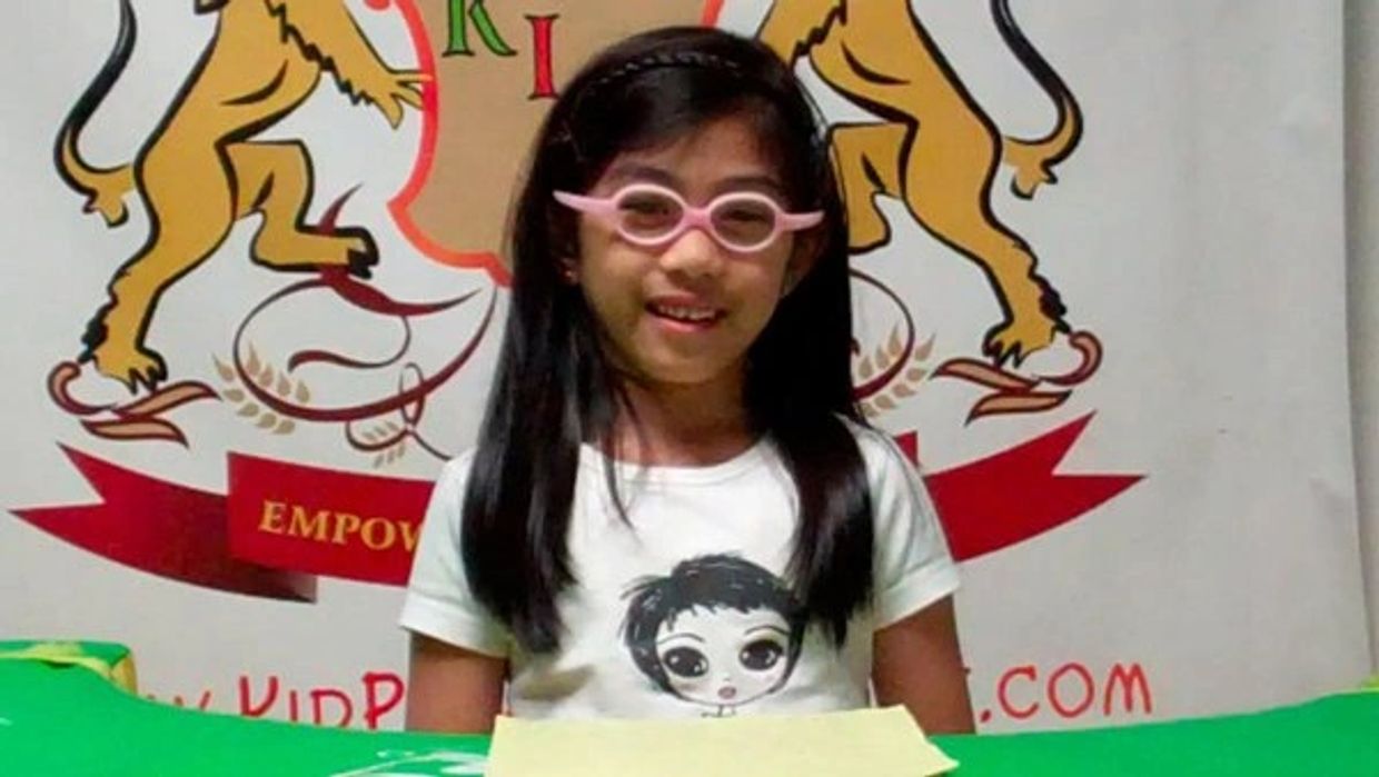 Young girl with pink glasses smiling in front of a colorful backdrop.