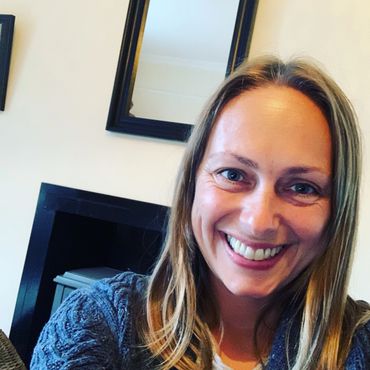 Smiling woman with blonde hair in cozy blue sweater indoors.