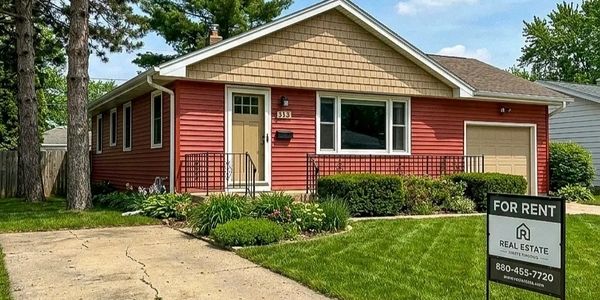 Single-story red house with a front yard and a 'For Rent' sign.