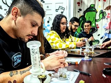 A group of people rolling joints around a table with cannabis-related items.