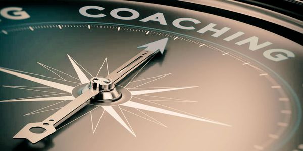 A close-up view of a compass pointing to the word "COACHING." It is sleek and modern.