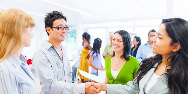 People shaking hands and smiling in a bright, modern office, engaging in a friendly conversation.