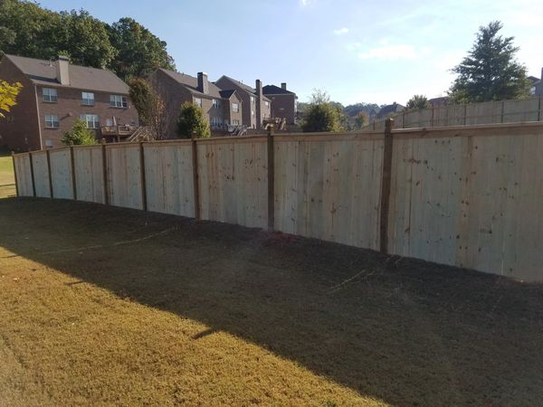 New wooden fence in a suburban backyard under a clear blue sky.