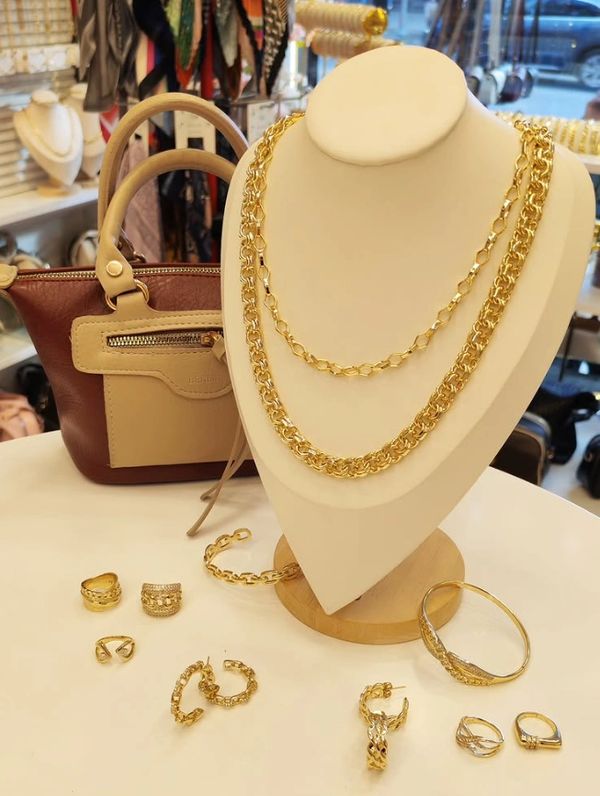 Gold jewelry set including necklaces, rings, bracelets, displayed with a handbag.
