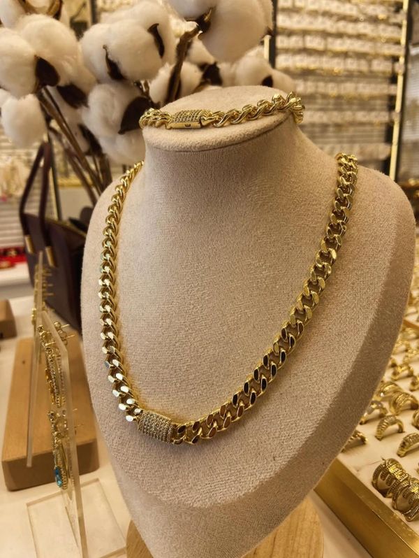 Gold chain necklace and bracelet displayed on a beige stand in a jewelry store.