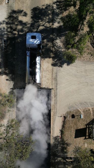 Aerial view of a steam train emitting smoke on a dirt track.