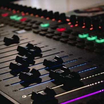 Close-up of an audio mixing console with illuminated sliders and knobs.