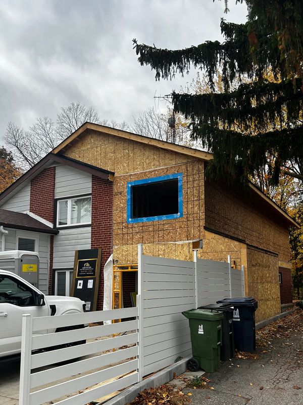 House under construction with wooden panels and a white fence.