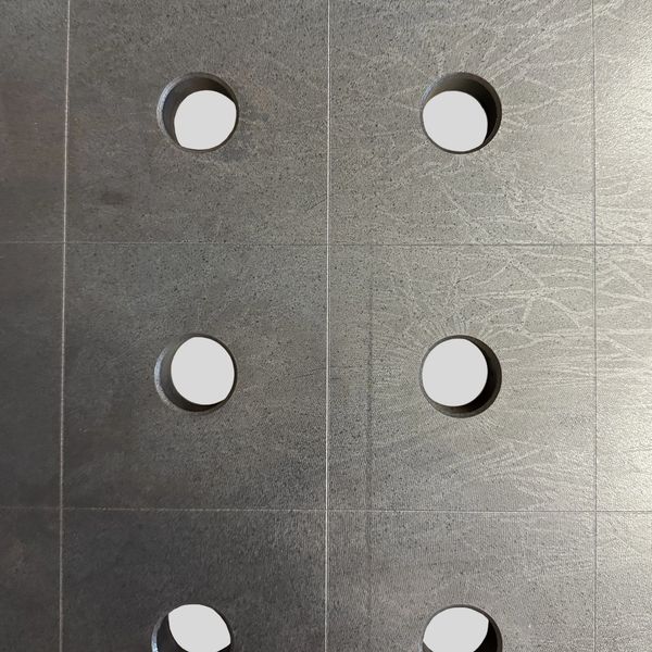 Gray textured surface with circular holes arranged in a grid.