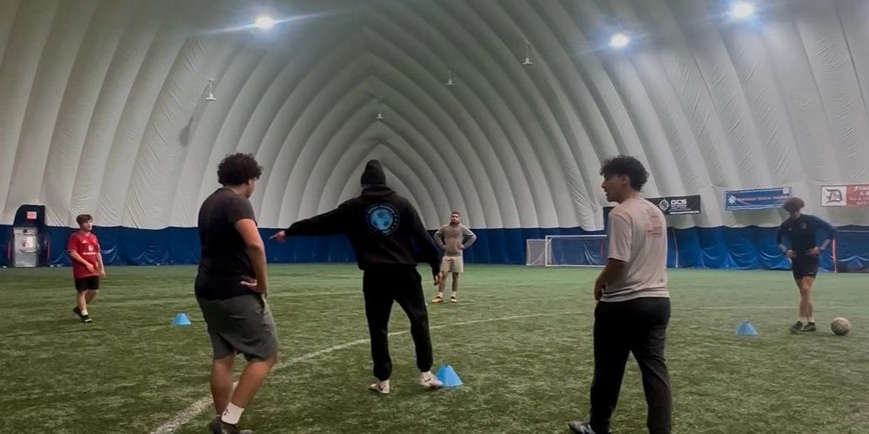 Four people on an indoor soccer field, one pointing.