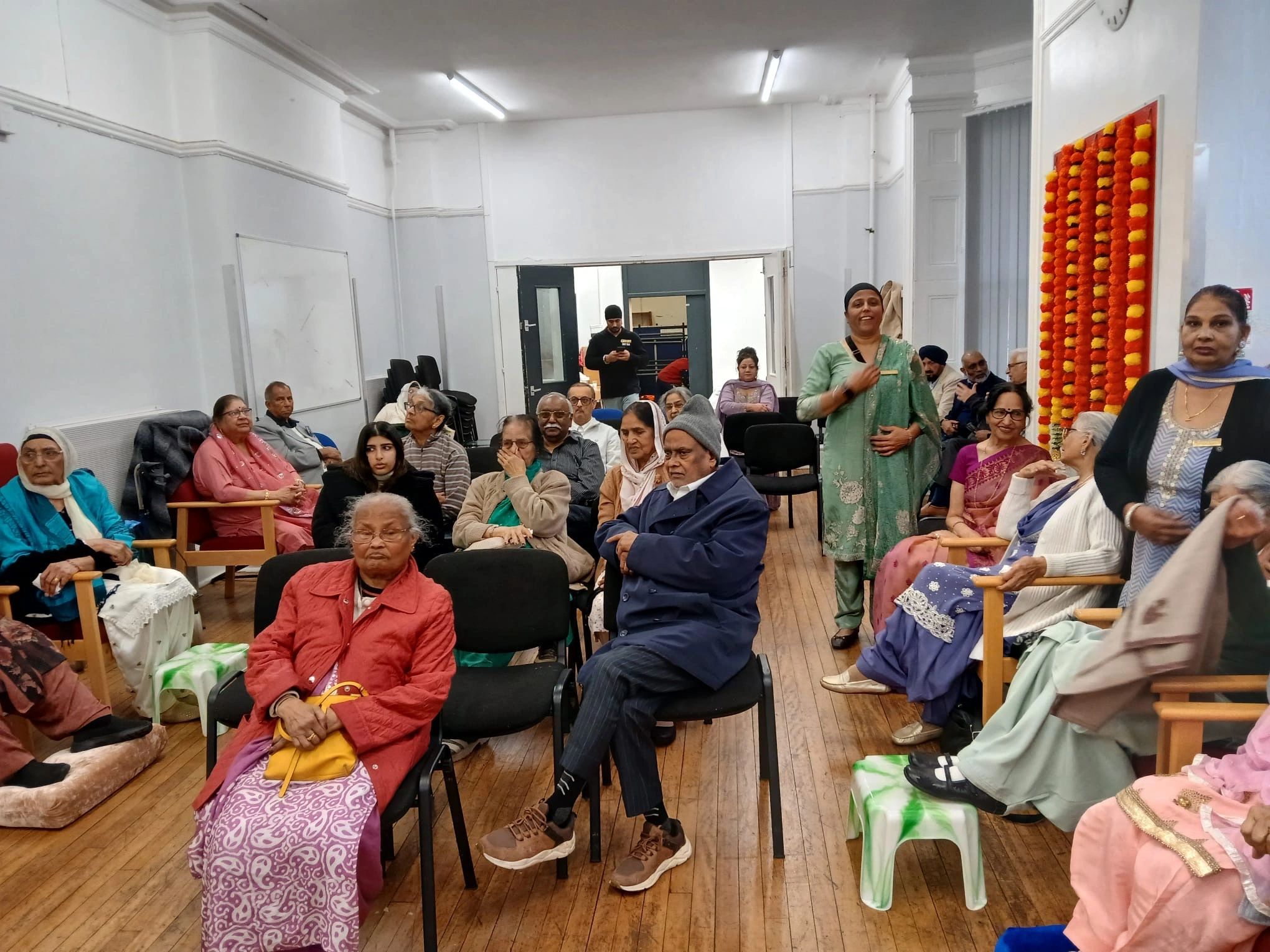 Group of elderly people gathered in a community room, some seated and others standing.
