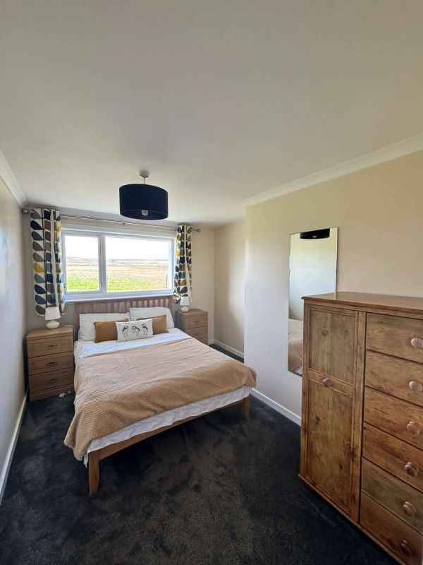 Cozy bedroom with wooden furniture and natural light from a large window.