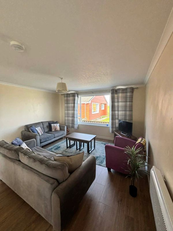 Cozy living room with neutral sofas, a purple armchair, and a window view of a red house.