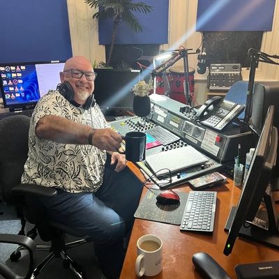 Man smiling and holding a mug in a radio broadcasting studio.