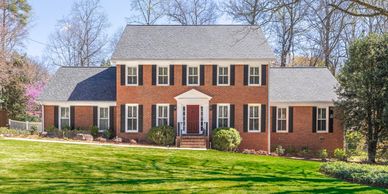 Large brick house with black shutters and a manicured lawn.