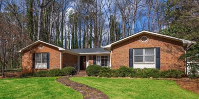 Single-story brick house with black shutters and a stone pathway surrounded by trees.