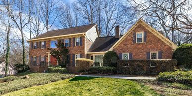 A large brick two-story house with an attached single-story section under a clear blue sky.