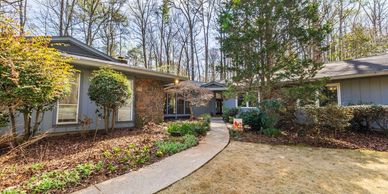 Modern house with a curved walkway and landscaped garden in a wooded area.
