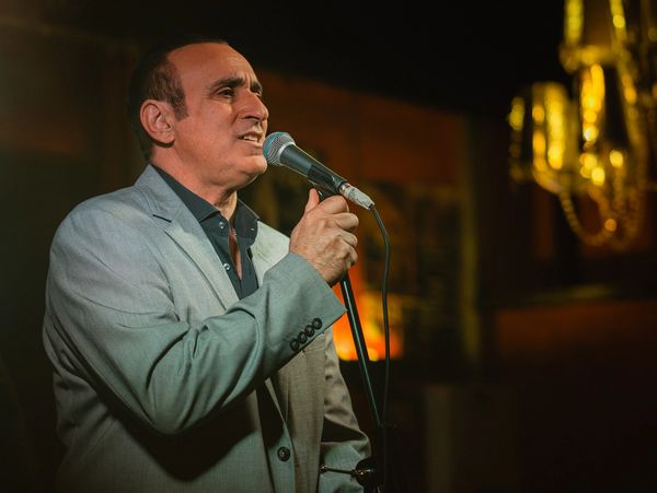 Man in suit passionately singing into a microphone on stage.