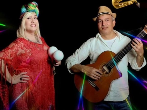 A woman in colorful headwrap with maracas and a man playing guitar.