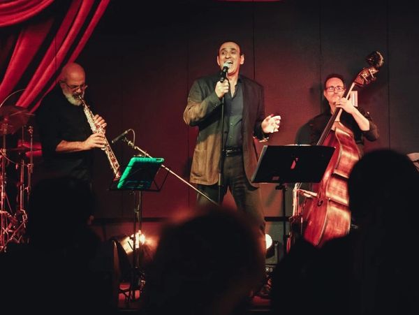 A jazz trio performs live on stage with a singer, saxophonist, and bassist.