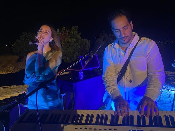 A woman singing and a man playing keyboard under blue lighting at night.