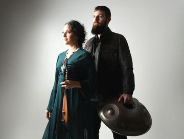 Two musicians holding unique instruments, standing in a studio with soft lighting.