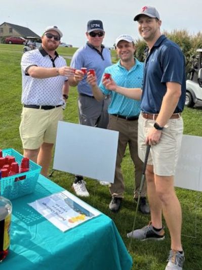 Four men toasting with small red cups on a golf course.