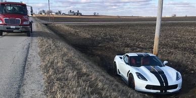 White sports car stuck beside a rural road with a truck nearby.