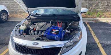 Car battery jump starter attached to a white Kia with the hood up.